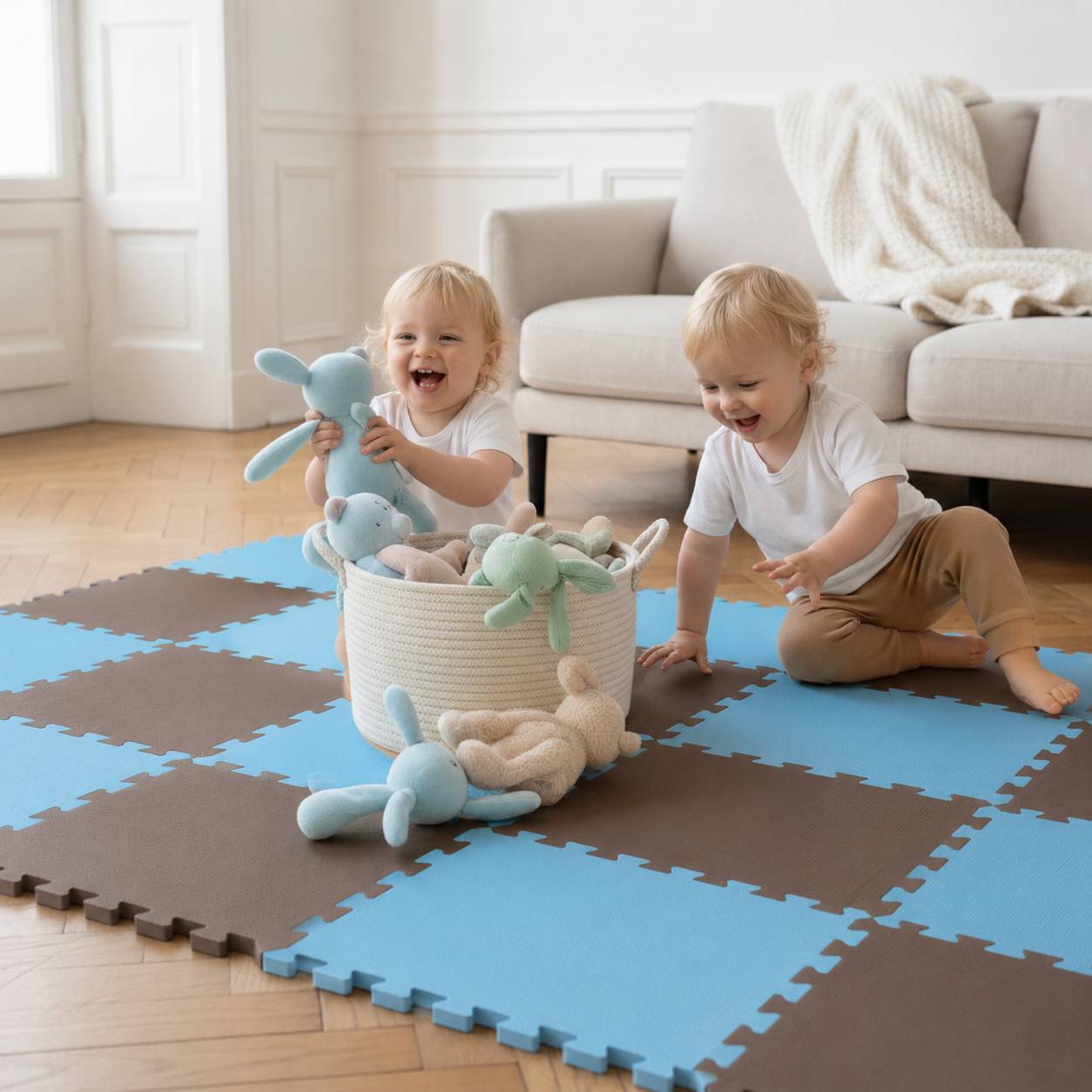 Zwei Kleinkinder spielen mit Kuscheltieren auf einer Schaumstoff-Puzzlematte in einem hellen Wohnzimmer.