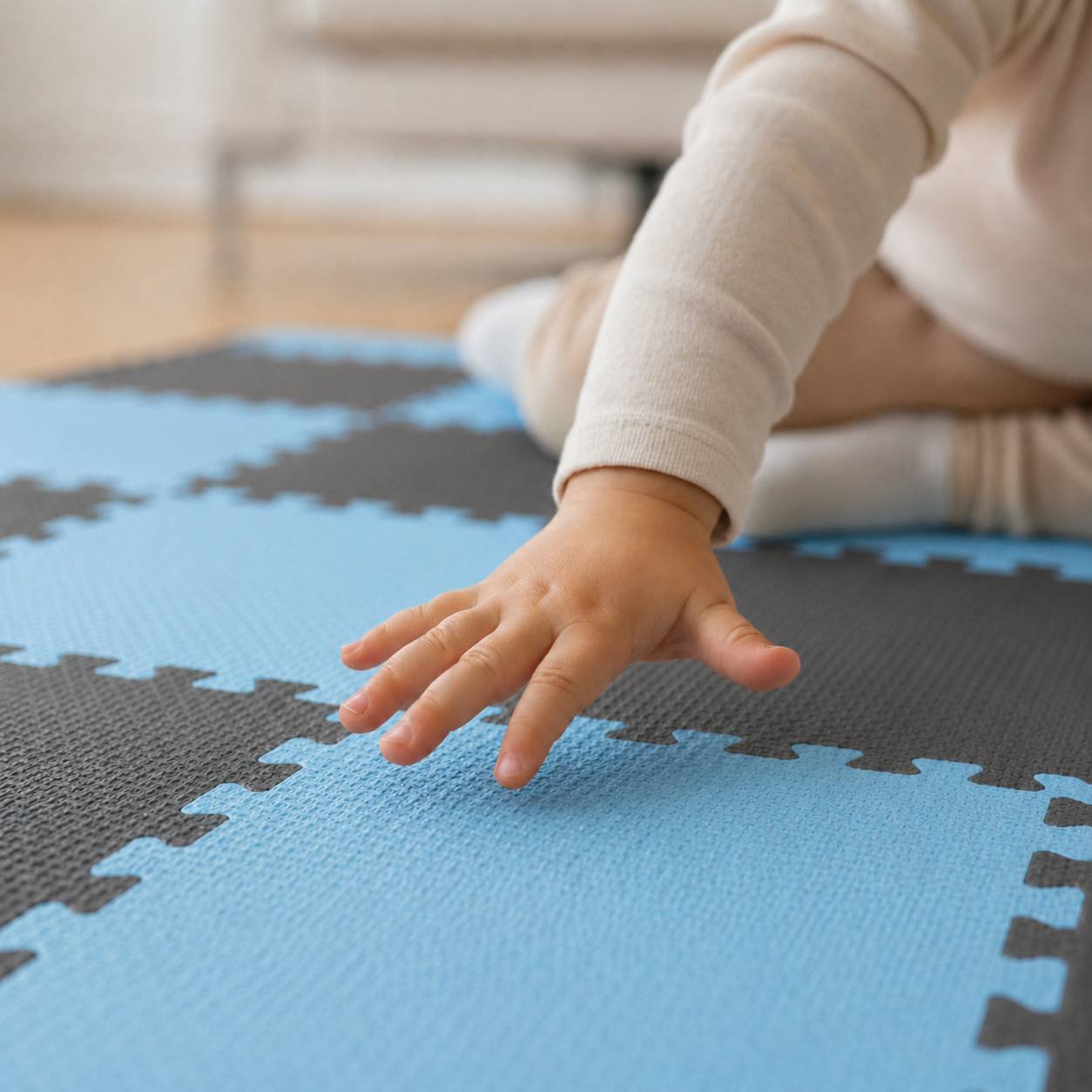 Nahaufnahme einer Babyhand, die eine blau-schwarze Schaumstoff-Spielmatte berührt, während das Baby auf dem Boden krabbelt.