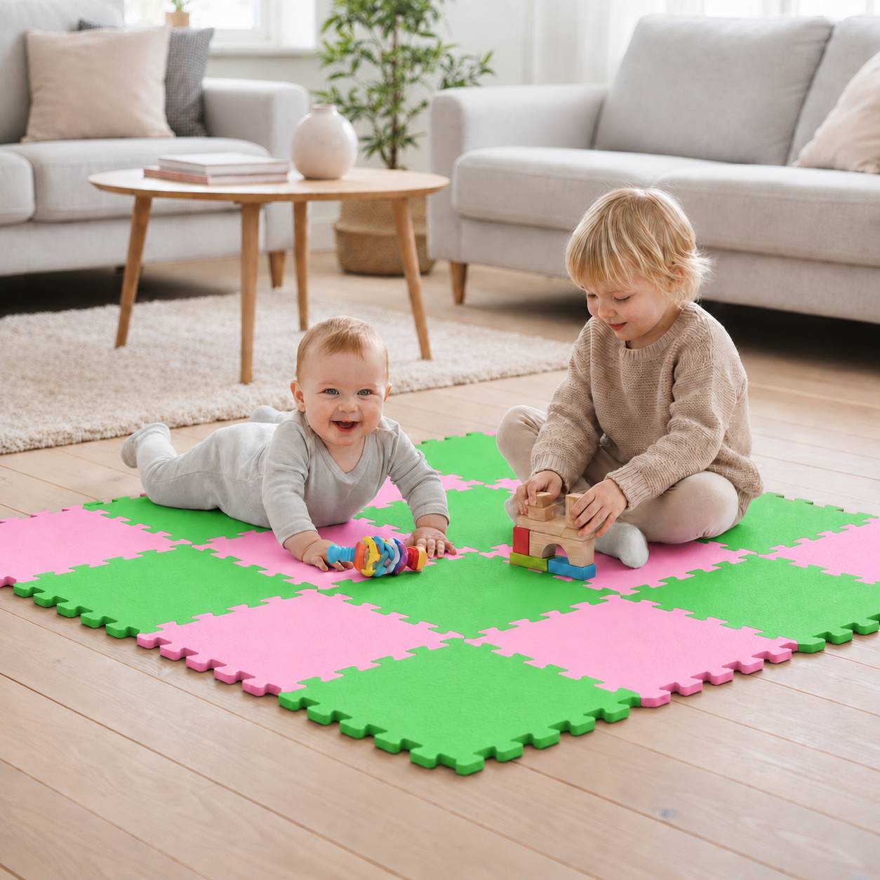Zwei kleine Kinder spielen mit Spielzeugen auf einer rosa-grünen Schaumstoffmatte in einem hellen Wohnzimmer.