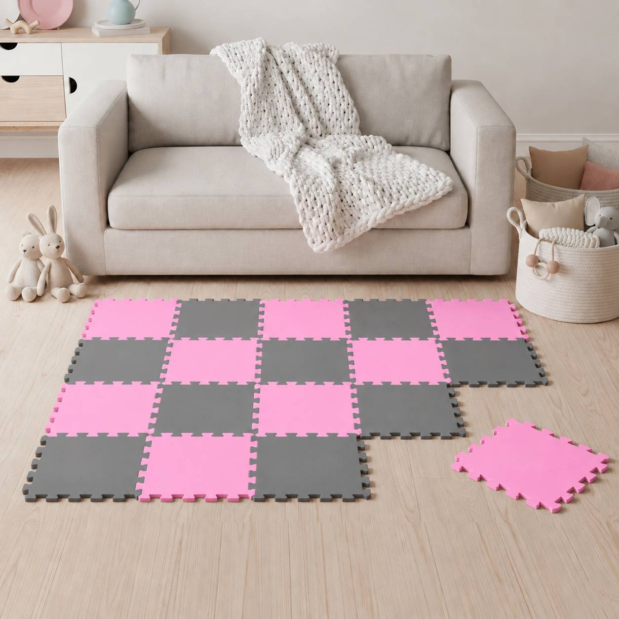 Wohnzimmer mit beigem Sofa und dicker Strickdecke, mit einer rosa und grauen Schaumstoff-Puzzlematte auf dem Boden mit einer lockeren Fliese in der Nähe.