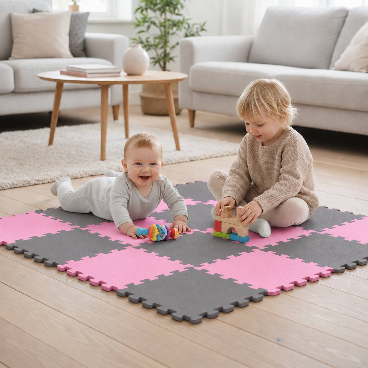 Zwei kleine Kinder spielen auf rosa und grauen Schaumstoffmatten in einem hellen Wohnzimmer, wobei eines liegt und das andere hölzerne Bausteine stapelt.