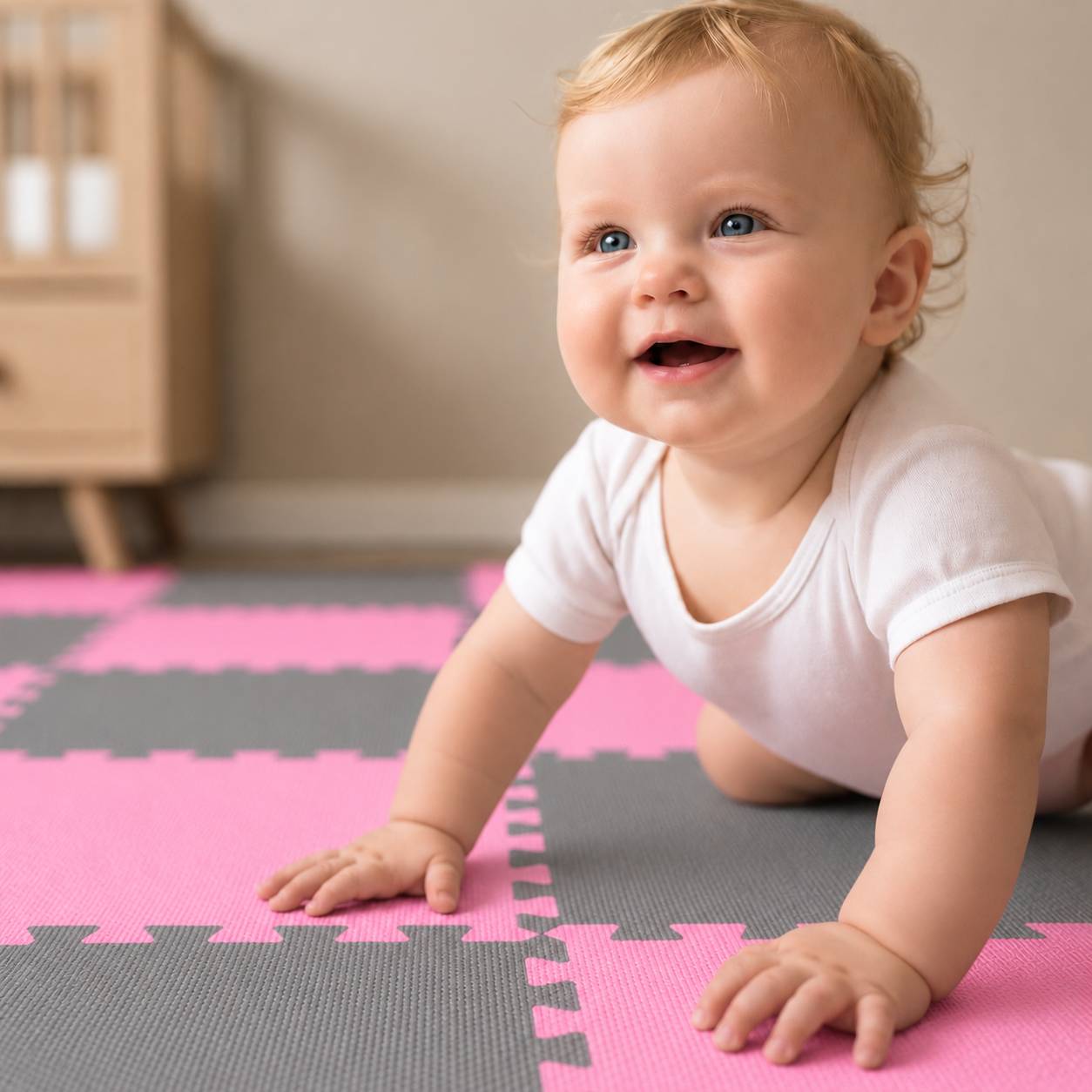 Ein lächelndes Baby, das auf einer rosa und grauen Schaumstoffmatte drinnen krabbelt.