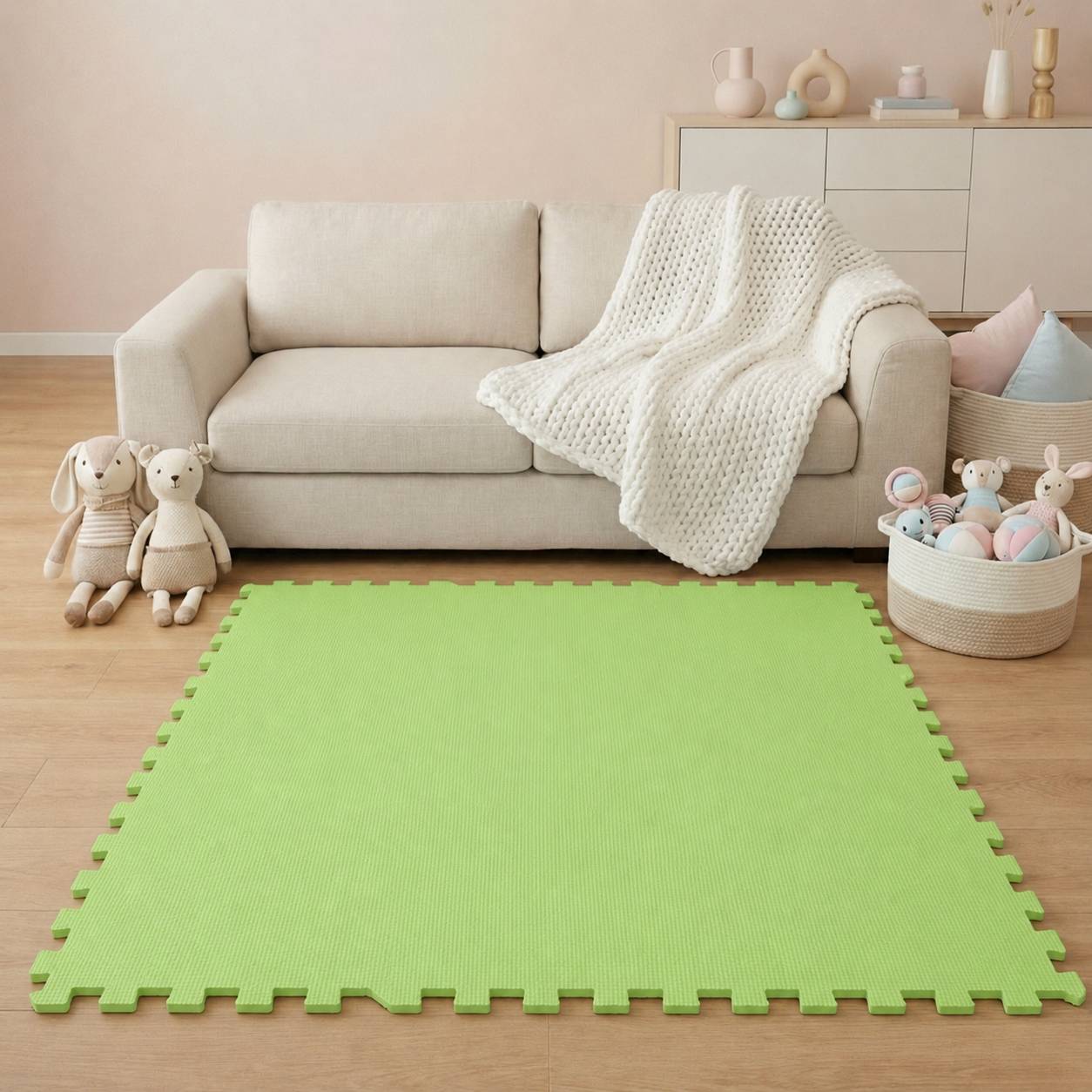 Ein beiges Sofa mit einer weißen Strickdecke steht hinter einer grünen Schaumstoff-Spielmatte, mit Kuscheltieren und einem Spielzeugkorb in einem ordentlichen Wohnzimmer.