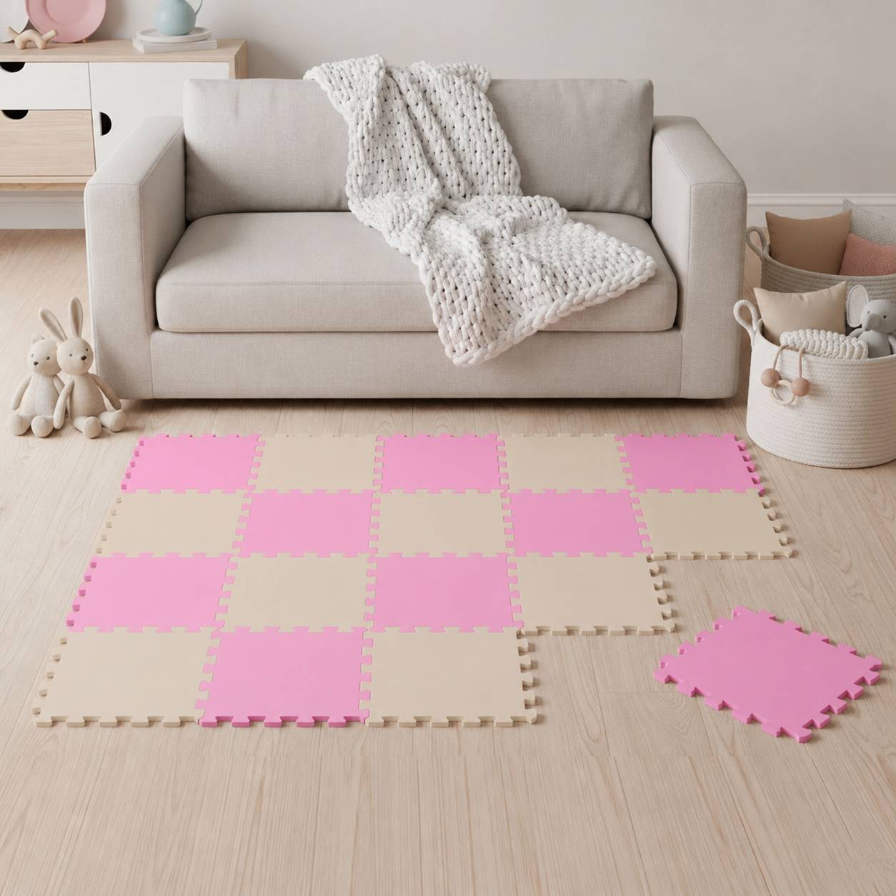 Wohnzimmer mit beigem Sofa und weißem Plaid, rosa-beige Schaumstoff-Spielmatte auf dem Boden, mit Körben und Stoffhasen in der Nähe.