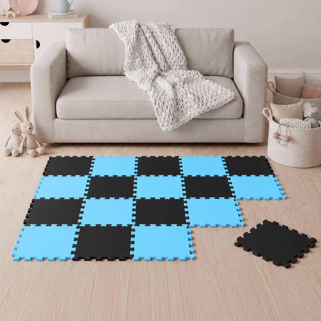 Wohnzimmer mit einem beigen Sofa und Spielzeugspeicher, plus ineinandergreifende schwarze und blaue Schaumstoff-Bodenfliesen, die in einem Schachbrettmuster auf dem Boden angeordnet sind.