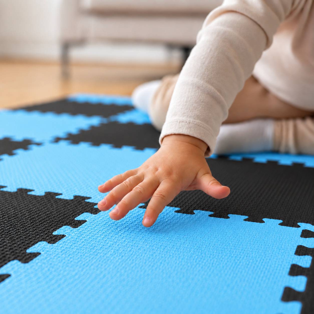 Nahaufnahme einer Kinderhand auf blauen und schwarzen Schaumstoff-Puzzlematten, was auf Spielen oder Krabbeln auf einem weichen Boden hindeutet.