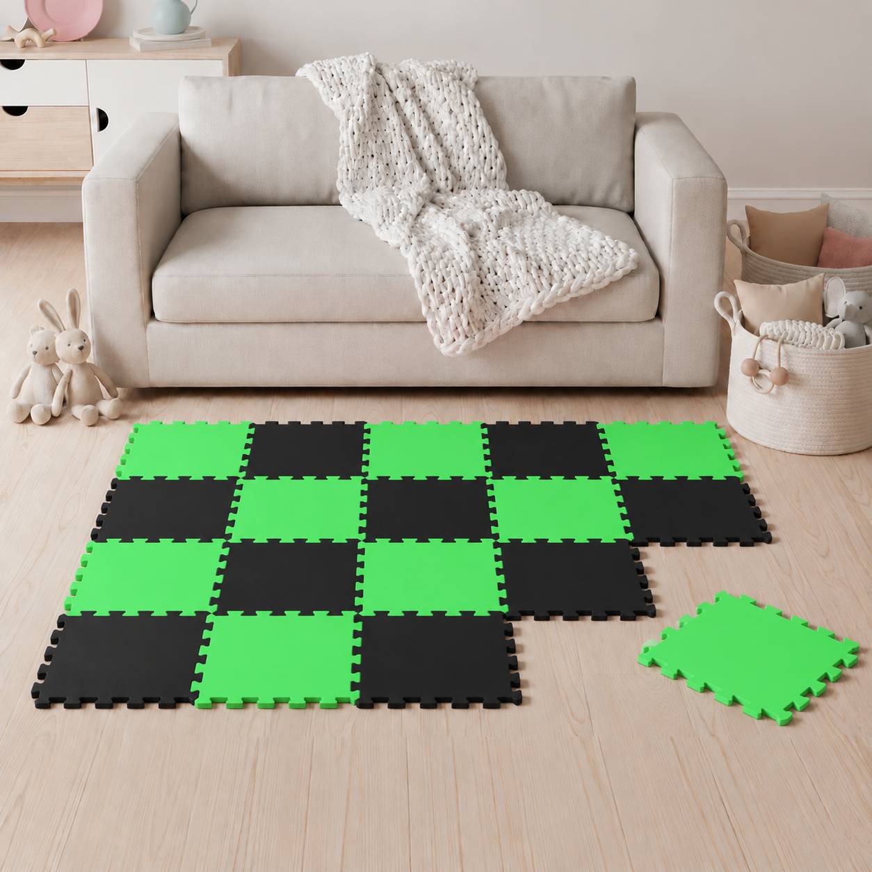 Wohnzimmer mit einem beige Sofa und einer Decke; schwarze und grüne verschlungene Schaumstoff-Bodentafeln bedecken den Boden, mit einer lose liegenden Fliese in der Nähe.