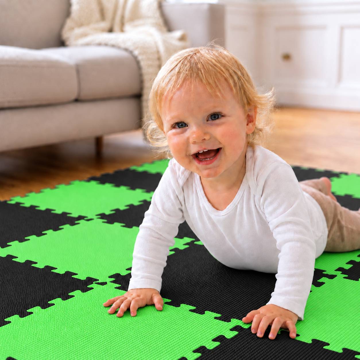 Ein lächelndes Baby krabbelt auf einer grün-schwarzen Schaumstoff-Spielmatte in einem Wohnzimmer.