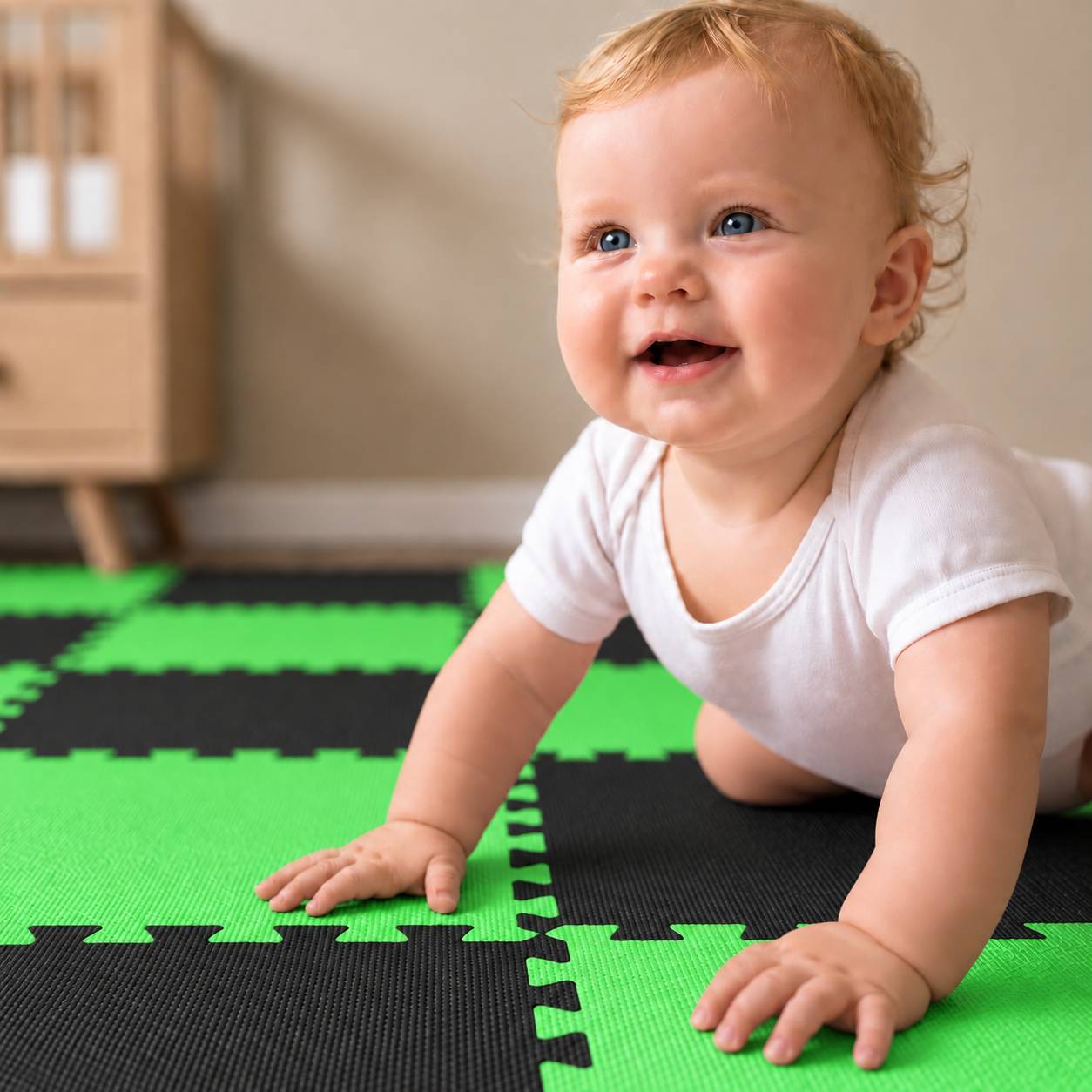 Lachendes Baby in weißem Strampler krabbelt auf grün-schwarzen Schaumstoff-Bodenschutzmattan drinnen.
