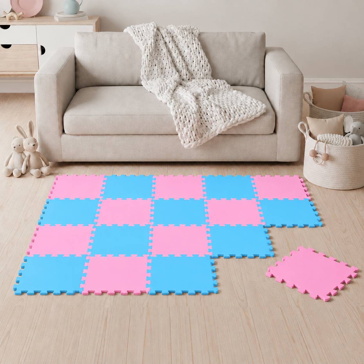 Spielzimmer mit beigem Sofa und Decke, mit einer rosa-blauen Schaumstoff-Puzzlematte auf dem Boden und Plüschkaninchen in der Nähe.
