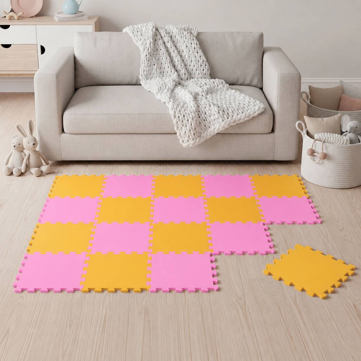 Spielzimmer mit beigem Sofa und gestrickter Decke; rosa und gelbe Schaumstoff-Puzzlematte bedeckt den Boden, mit Spielzeug und Aufbewahrungskörben in der Nähe.