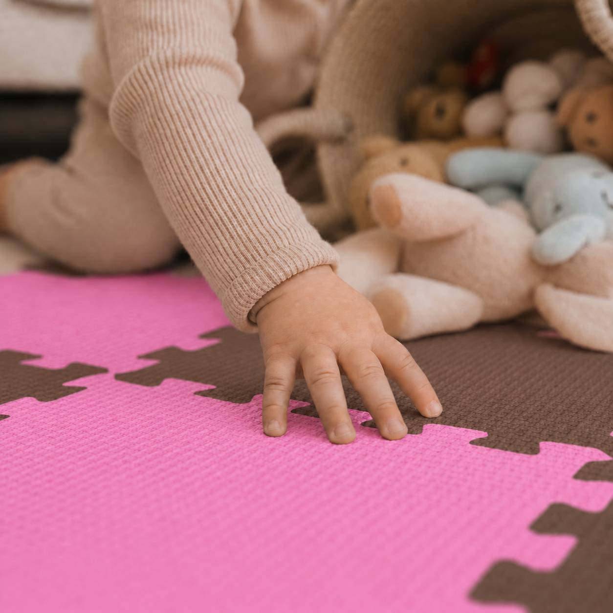 Hand eines Kindes berührt eine rosa Schaumstoff-Puzzlematte neben Plüschtieren auf dem Boden.