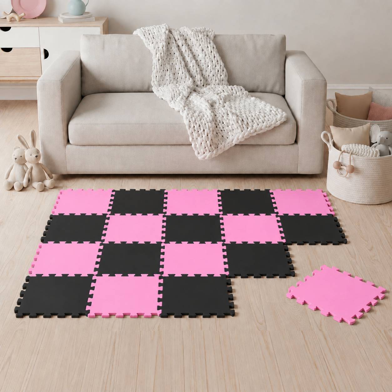 Wohnzimmer mit einem beigen Sofa und einer rosa-schwarzen ineinandergreifenden Schaumstoff-Spielmatte auf dem Boden, mit einer lockeren Fliese in der Nähe.