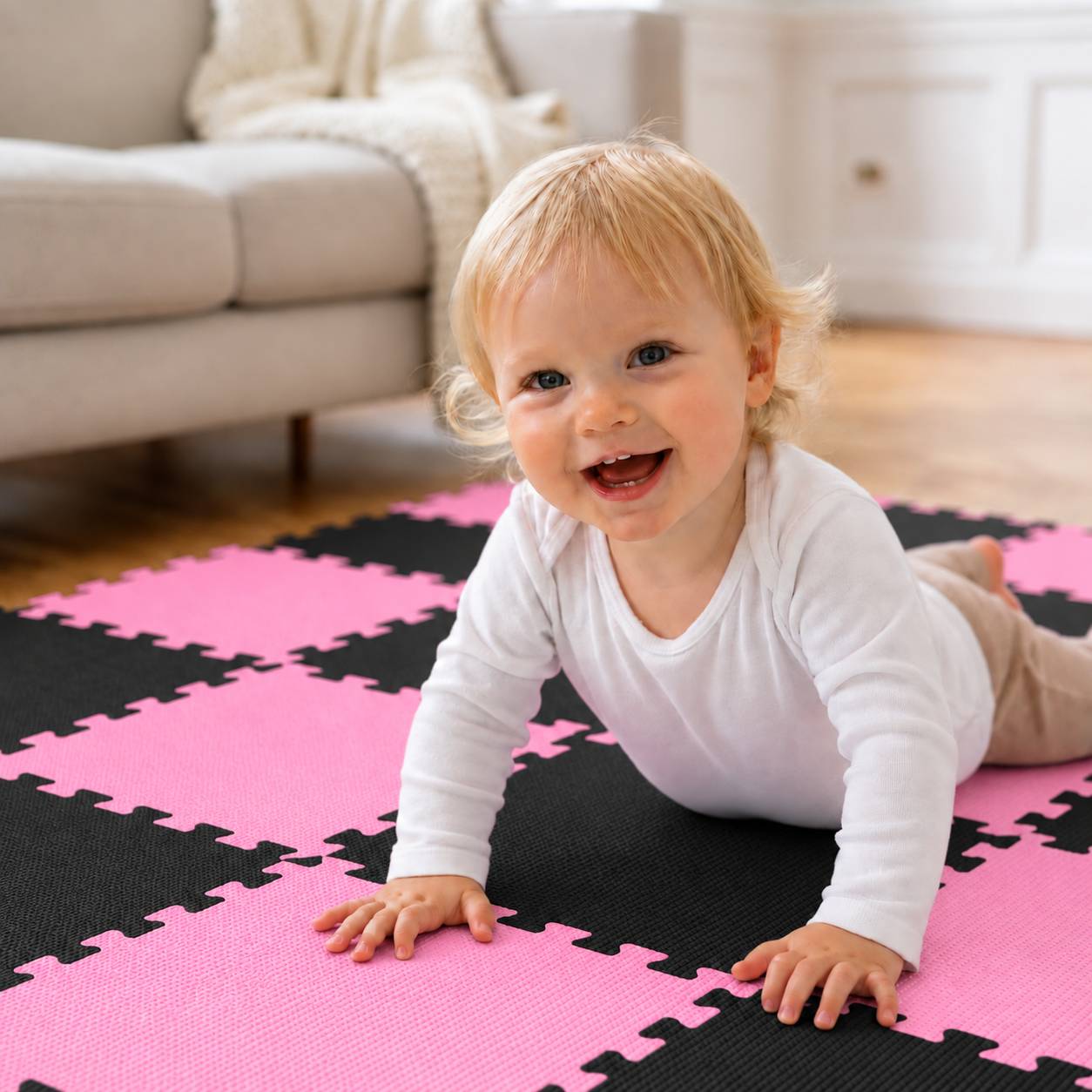 Ein lächelndes Baby kriecht auf einer rosa und schwarzen Schaumstoff-Spielmatte in einem hellen Wohnzimmer.