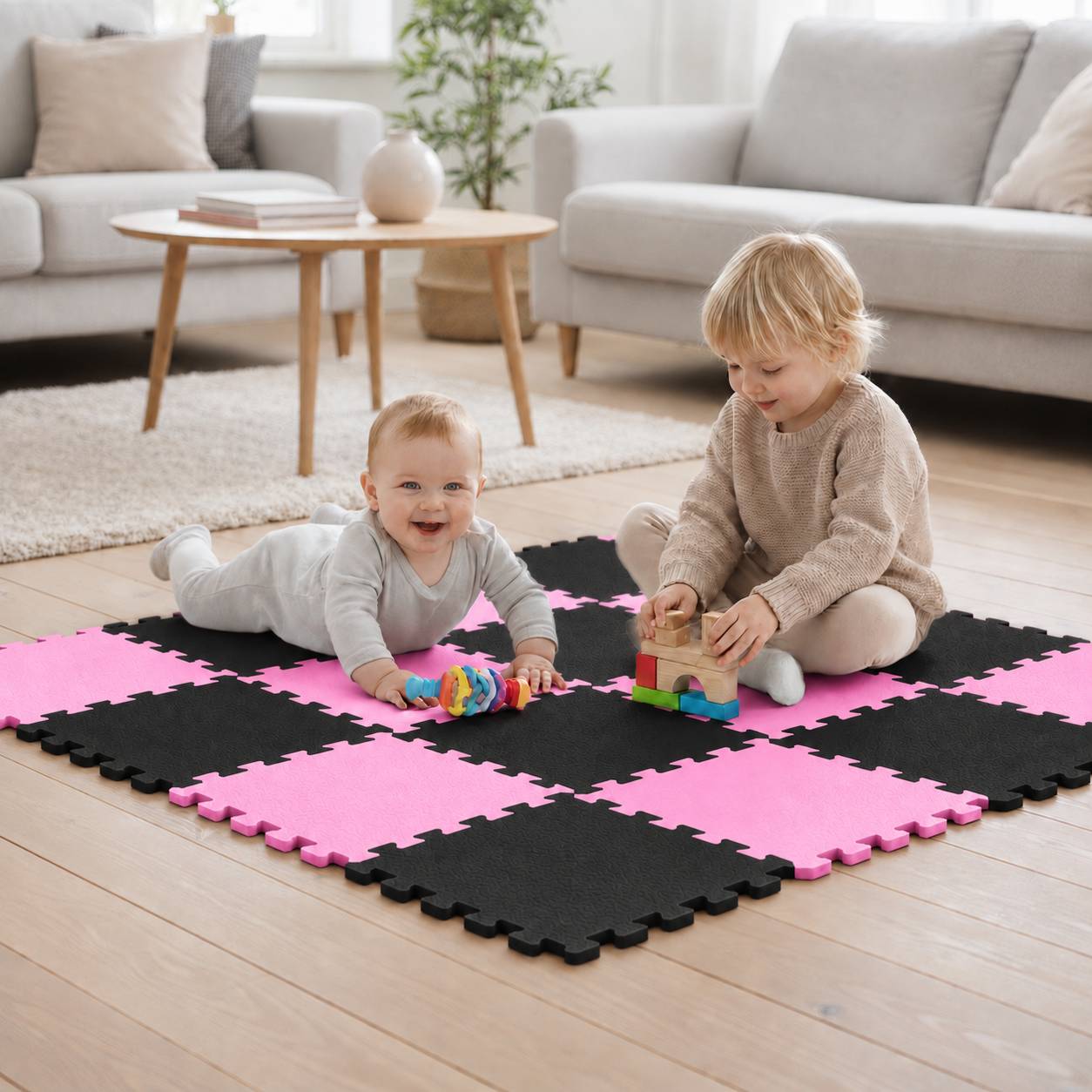 Zwei kleine Kinder spielen auf einer schwarz-rosa Schaumstoffmatte in einem Wohnzimmer, wobei eines liegt und lächelt, während das andere mit Blöcken baut.