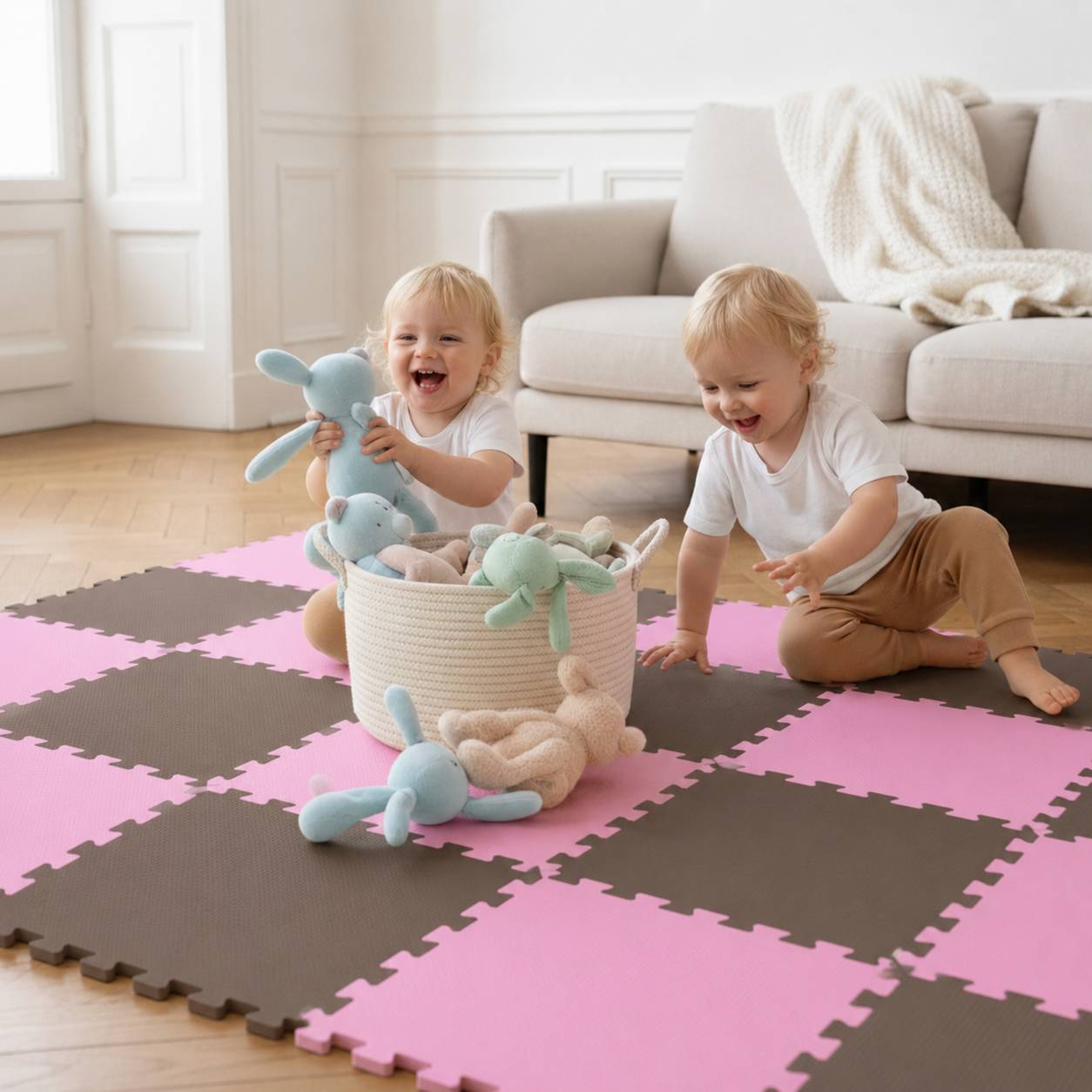 Zwei Kleinkinder spielen auf einer rosa-braunen Schaumstoffmatte, lächeln und halten Plüschhäschen neben einem Spielzeugkorb in einem hellen Wohnzimmer.