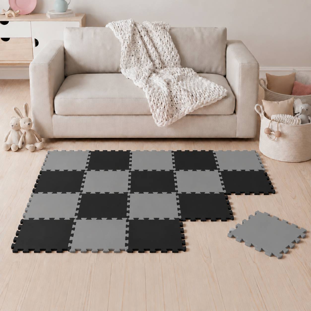 Gemütliches Wohnzimmer mit einem beige Sofa, gestrickter Wurfdecke und schwarzgrauer Schaumstoff-Puzzlematte auf dem Boden, mit einer losen Mattenkachel daneben.