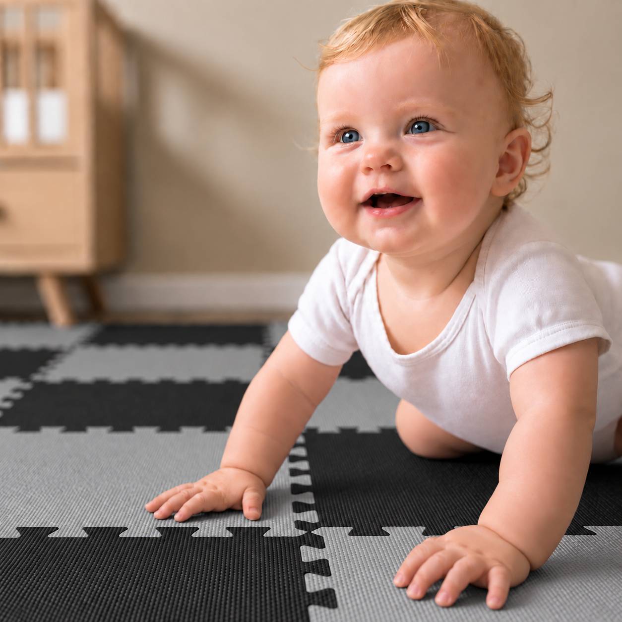 Lachendes Baby, das auf einer schwarzgrauen Schaumstoff-Spielmatte in Innenräumen krabbelt.