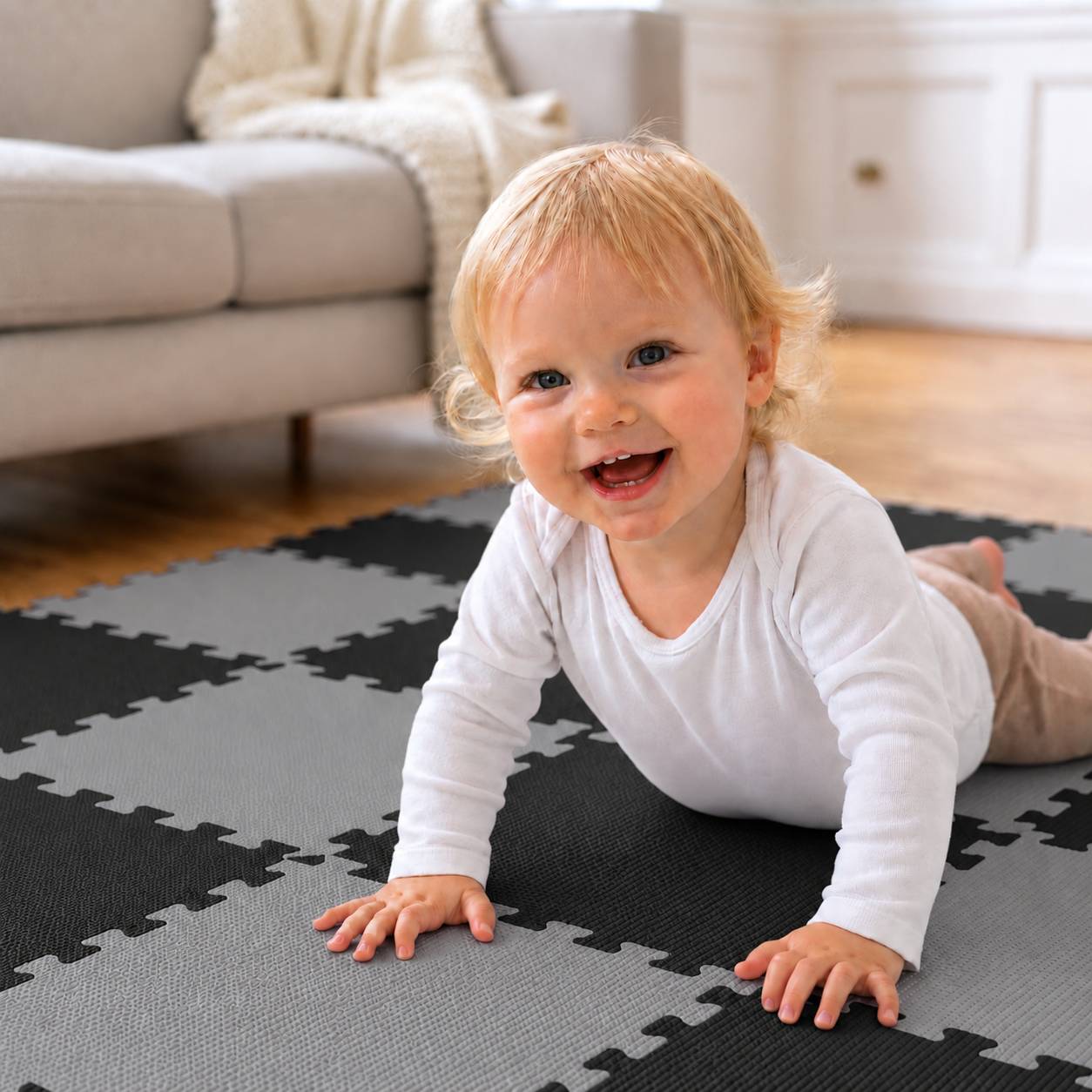 Lächelndes Baby, das auf einer schwarz-grauen Schaumstoff-Spielmatte in einem hellen Wohnzimmer krabbelt.