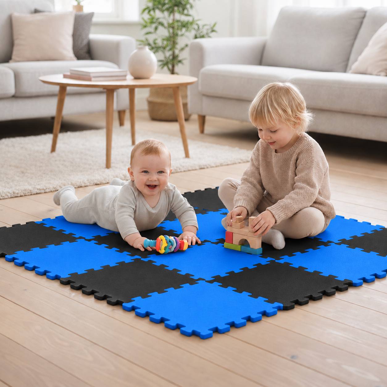Zwei Kinder spielen auf blauschwarzen Schaumstoffmatten in einem Wohnzimmer, eines liegt mit einem Spielzeug und eines stapelt Bausteine.