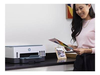 Eine Person steht neben einem Drucker und hält ein gedrucktes Foto, während auf dem Schreibtisch Familienfotos und ein Drucker stehen.