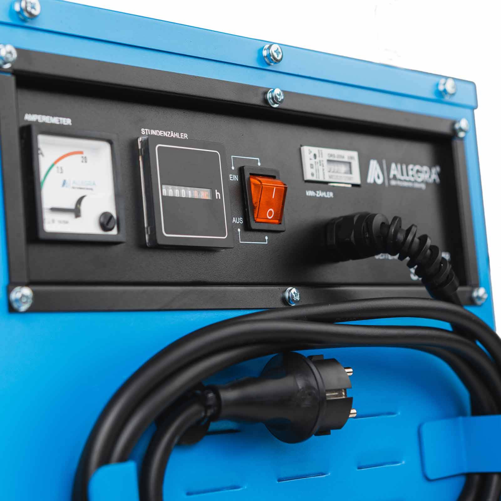 Nahaufnahme eines tragbaren elektrischen Schaltschranks mit einem Amperemeter, einem Betriebsstundenzähler und einem orangefarbenen Ein-/Ausschalter, sowie aufgewickelten Stromkabeln und einem Stecker.