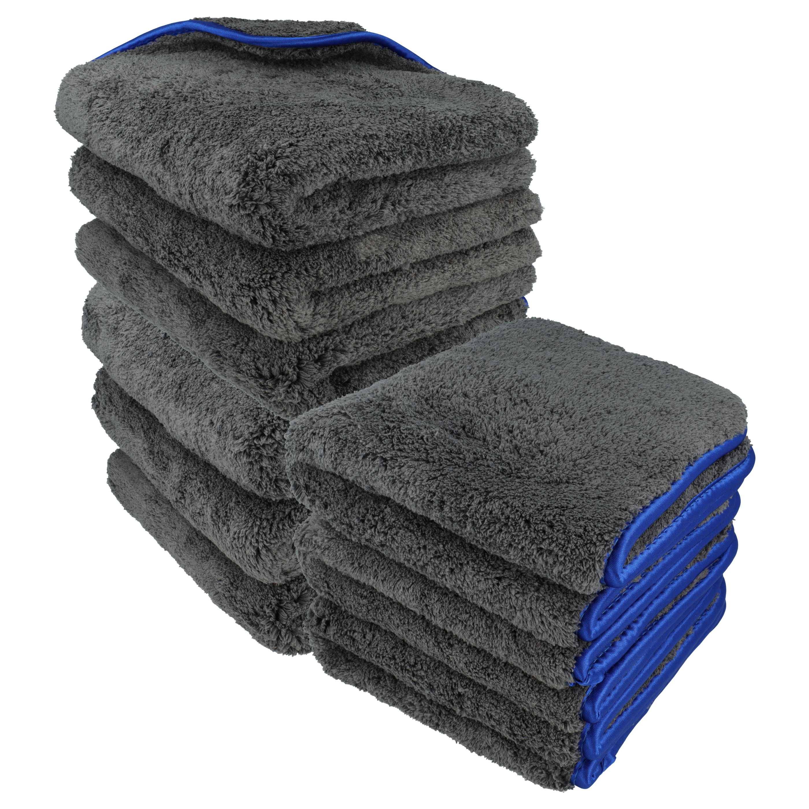 Ein Stapel dunkelgrauer, fluffiger Handtücher mit blauen Kanten, sauber gefaltet und in zwei Haufen angeordnet.