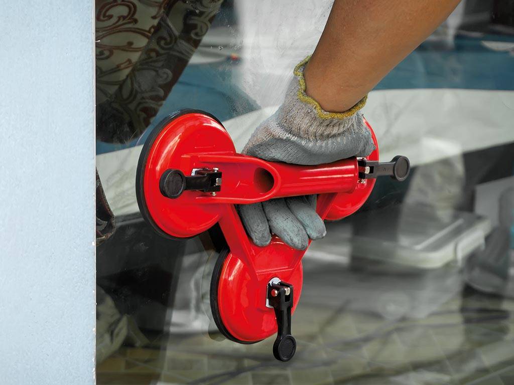 Behandschuhte Hand, die einen roten Dreibecher-Glassaugenheber gegen ein Fenster oder eine Glaspanel hält.