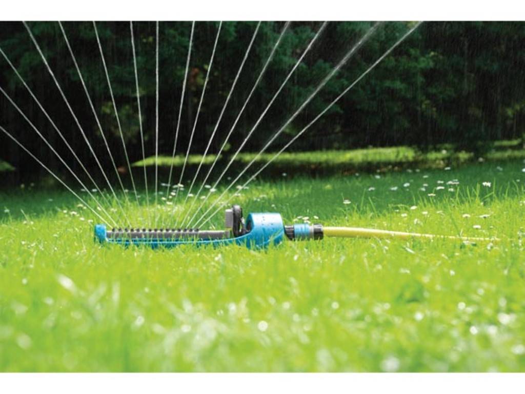 Ein Rasensprenger sprüht Wasser in einem Grasgarten, wobei bogenförmige Wasserstrahlen über das Gras verteilt sind.