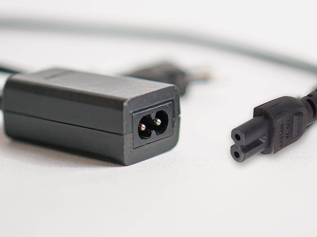 Eine Nahaufnahme eines schwarzen Netzadapters mit einem Zweipinnenstecker, der von seiner Buchse getrennt ist und zeigt das Anschlussende und die Vorderseite des Adapters.