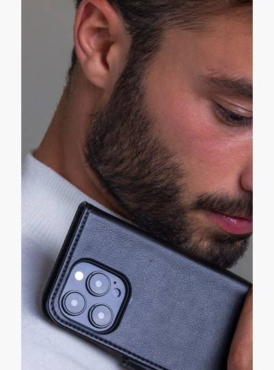 Nahaufnahme eines Mannes, der ein schwarzes Smartphone mit dreifacher Rückseite-Kamera gegen seine Wange hält und dabei einen Teil seines Gesichts und seines Ohrs zeigt.