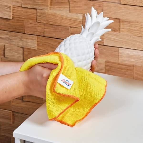 Hand wischt ein weißes ananasförmiges Ornament mit einem gelben Mikrofasertuch.