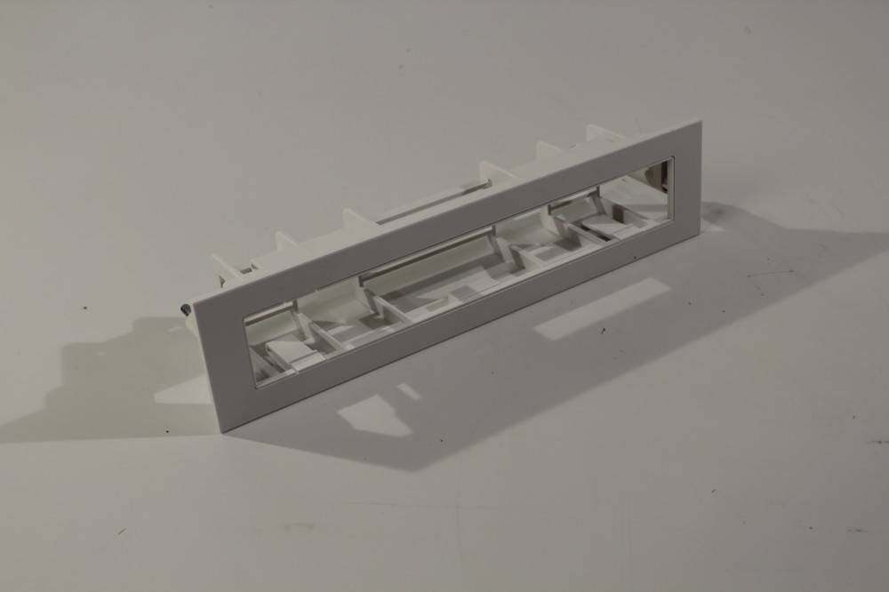 Eine rechteckige weiße Kunststoff-Lüftungsblende mit Lamellen, die für den Luftstrom in Belüftungssystemen konzipiert ist und auf einer ebenen Oberfläche positioniert wird.