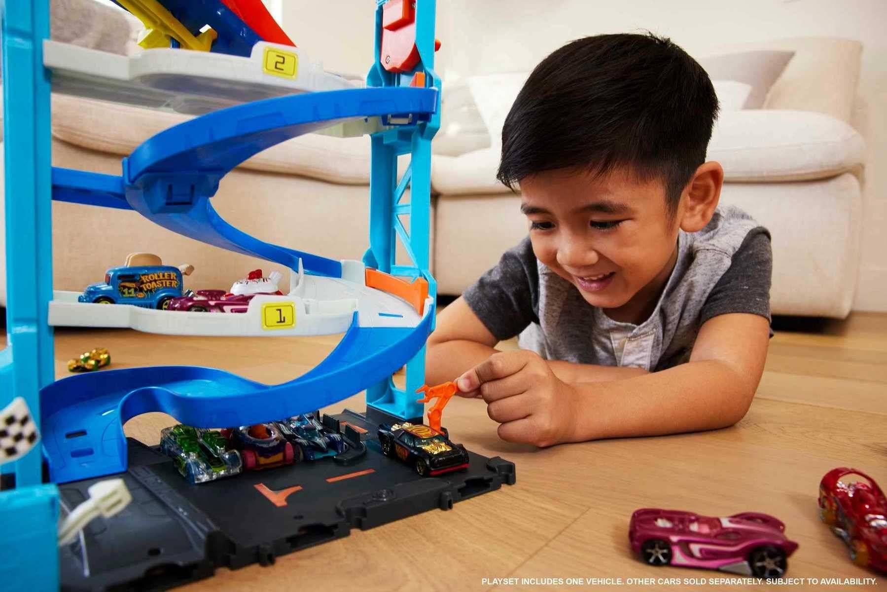 Kleiner Junge spielt mit Spielzeugautos neben einer blauen mehrstöckigen Autobahn-Rampenbahn im Wohnzimmer.