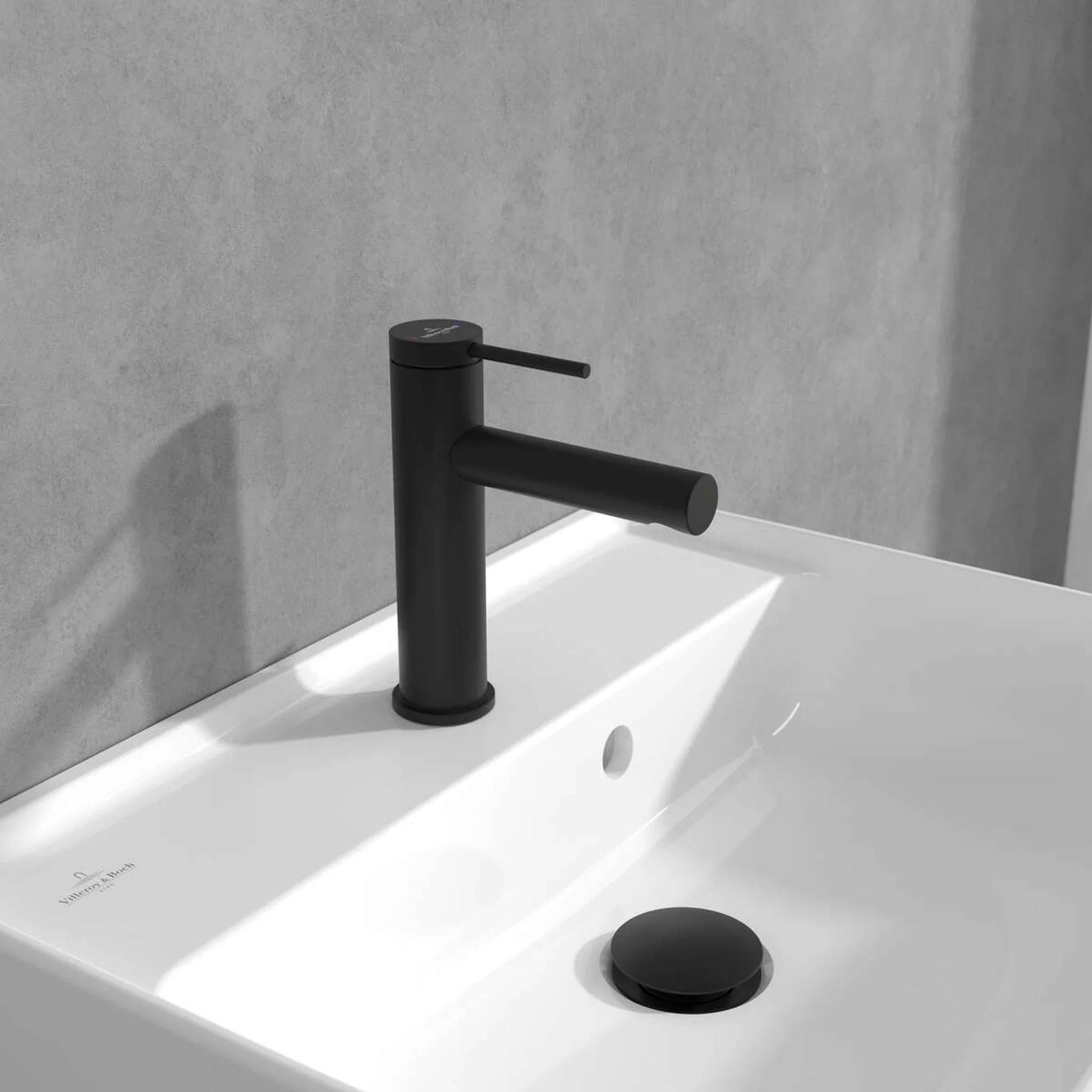 Matte schwarzer Einhebel-Badezimmerhahn über einem weißen Waschbecken mit schwarzem Ablaufstopfen vor einer grauen Wand.
