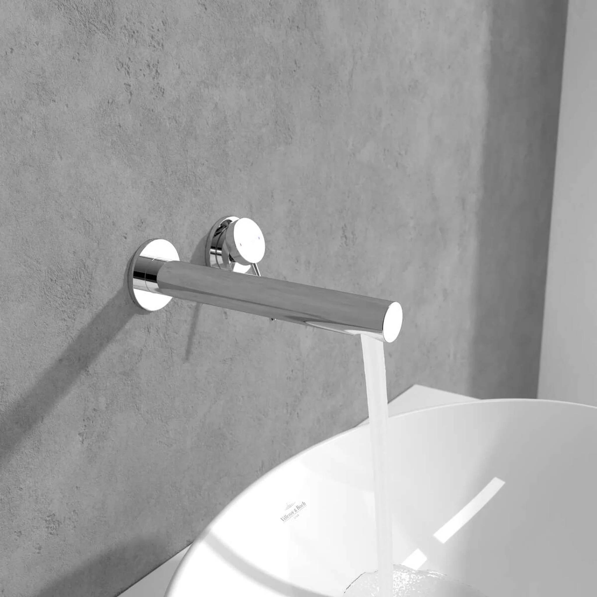 Wasser fließt aus einem modernen verchromten Wandarmatur in ein weißes Waschbecken an einer grauen Betonwand.