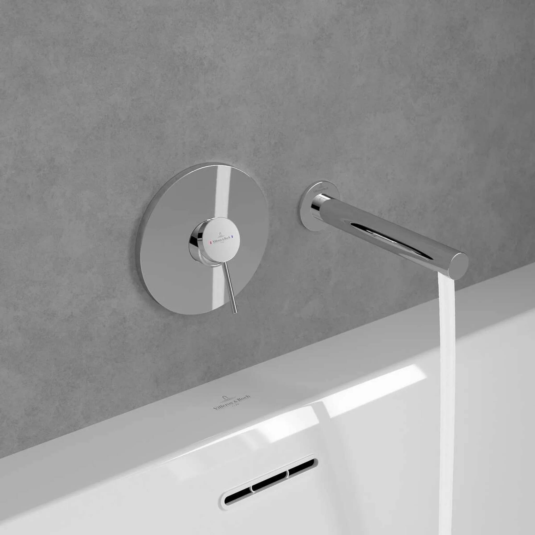Moderner Badezimmerhahn und wandmontierte Steuerung füllen eine weiße Badewanne gegen eine grau geflieste Wand.