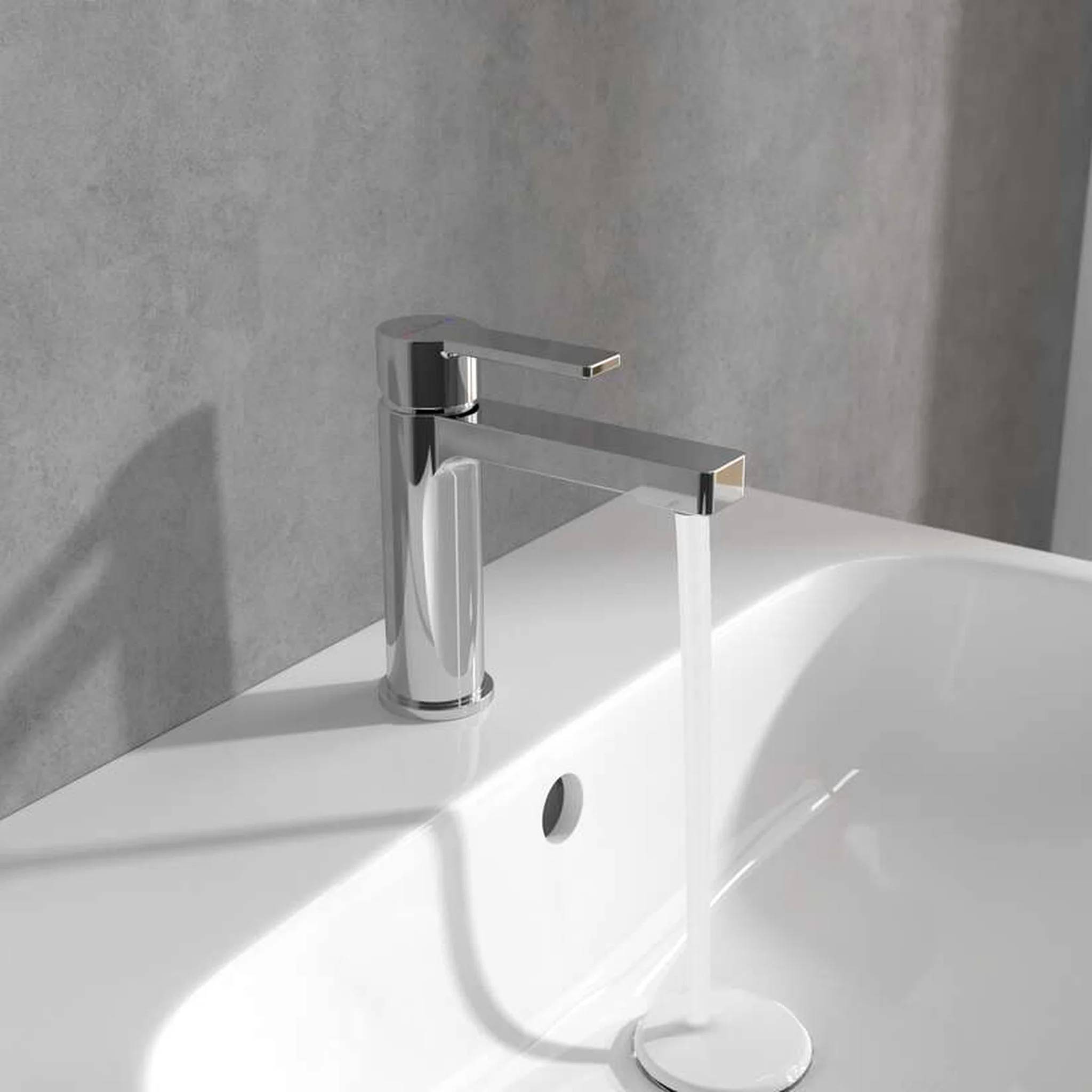 Verchromter Einhebel-Badezimmerhahn mit fließendem Wasser in ein weißes Waschbecken vor einer grauen Wand.