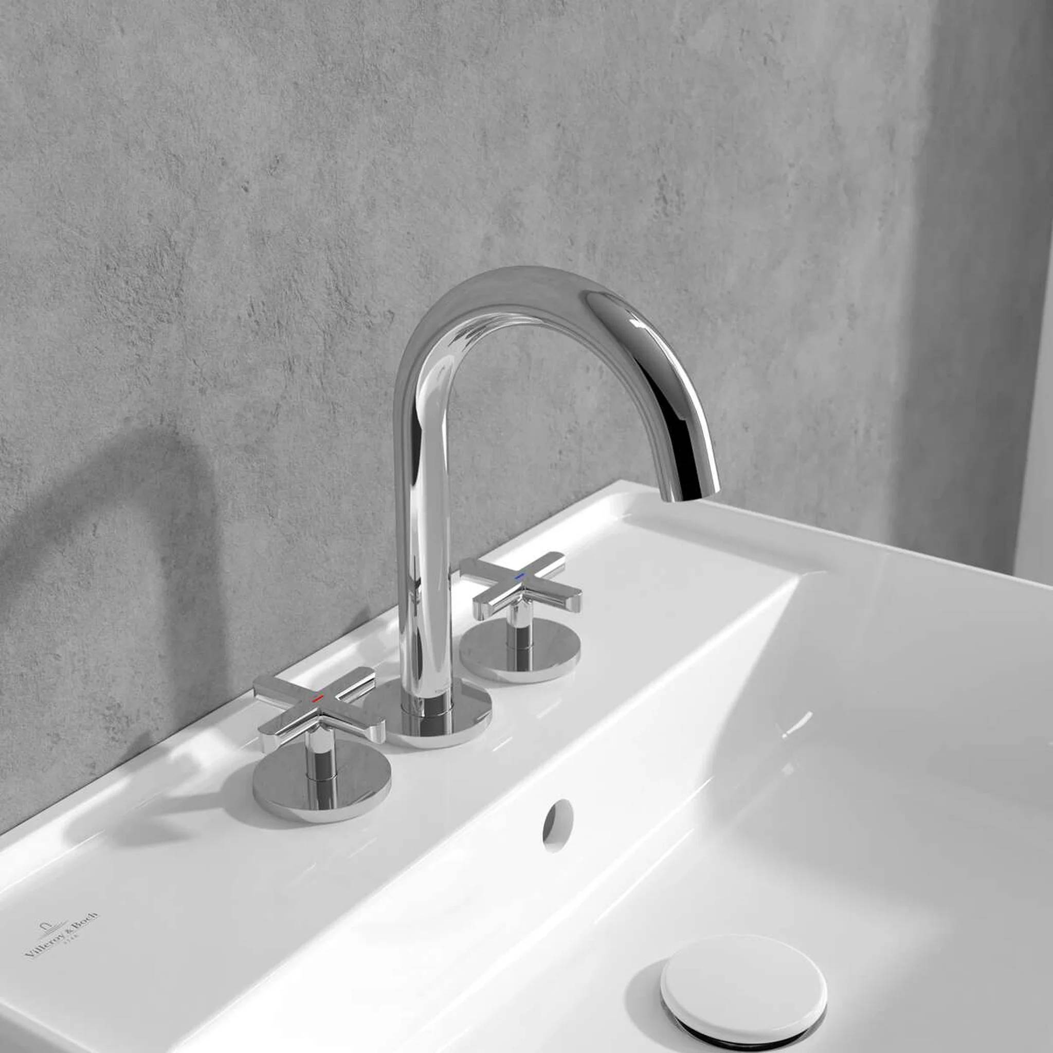Chrom-Wasserhahn mit separaten heißen und kalten Kreuzhebeln auf einem weißen Waschbecken vor einer grauen Wand.