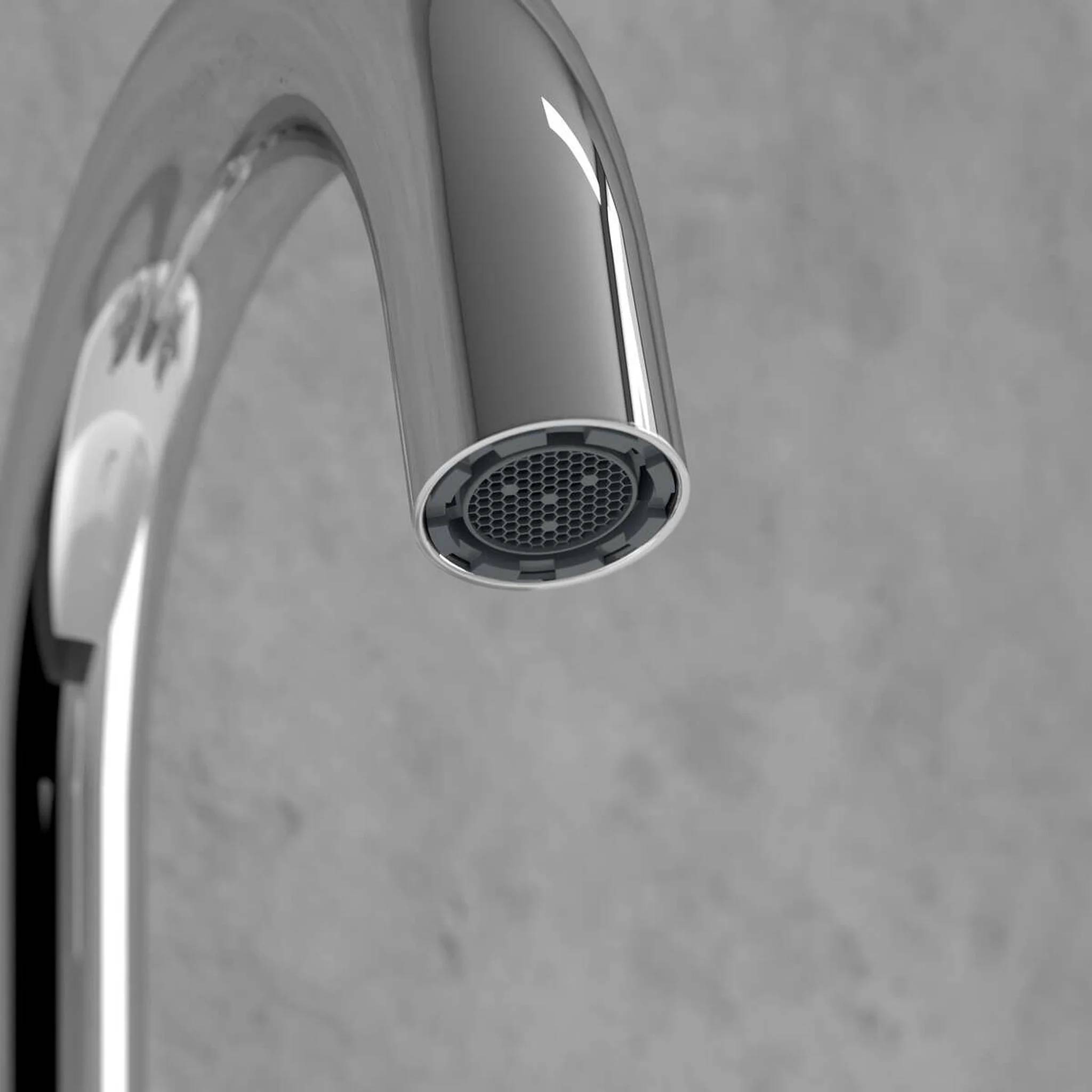Nahaufnahme einer verchromten Wasserhahn-Auslauföffnung vor grauem Hintergrund.