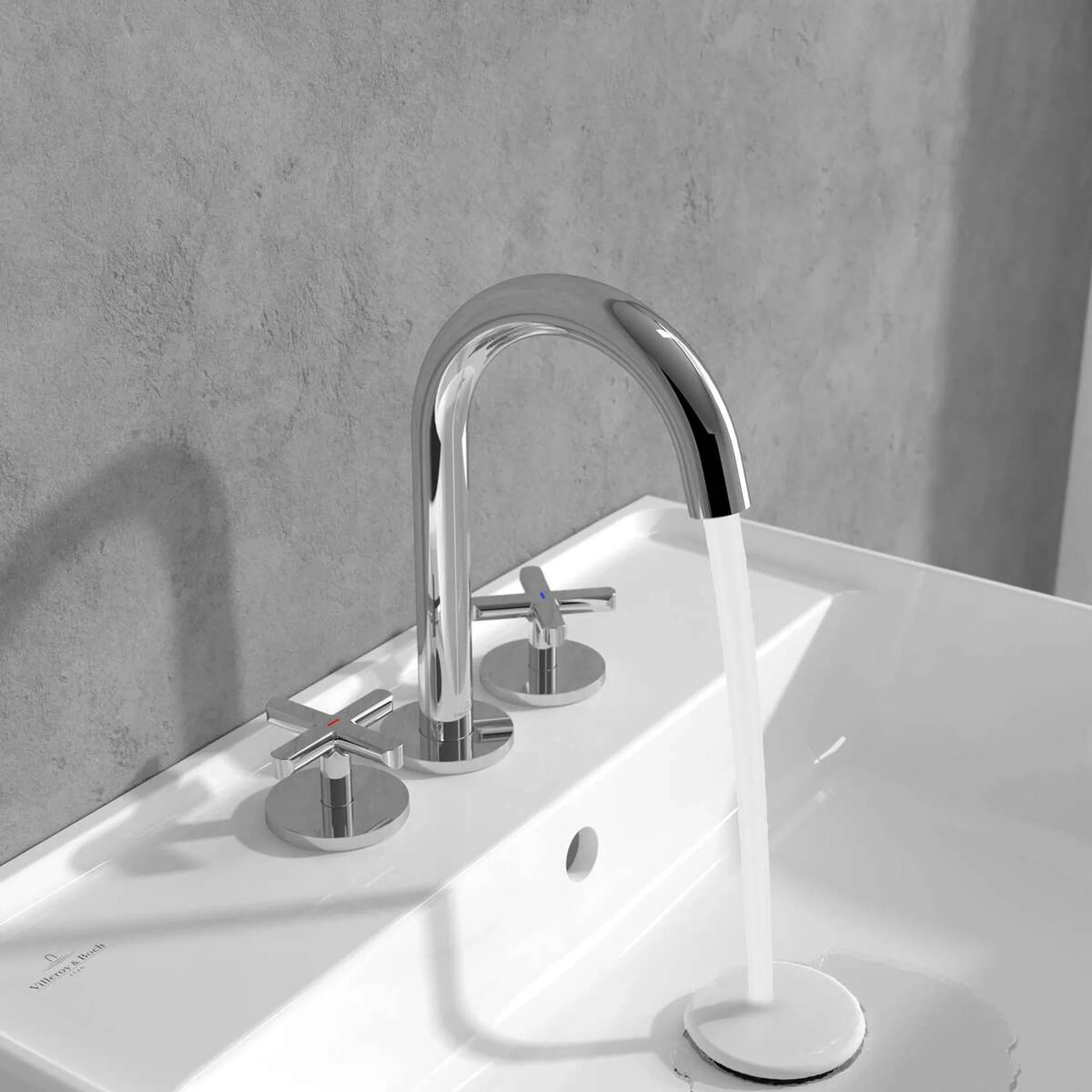 Modernes weißes Waschbecken mit Chromarmatur mit fließendem Wasser und zwei passenden Griffen vor grauem Wandhintergrund.
