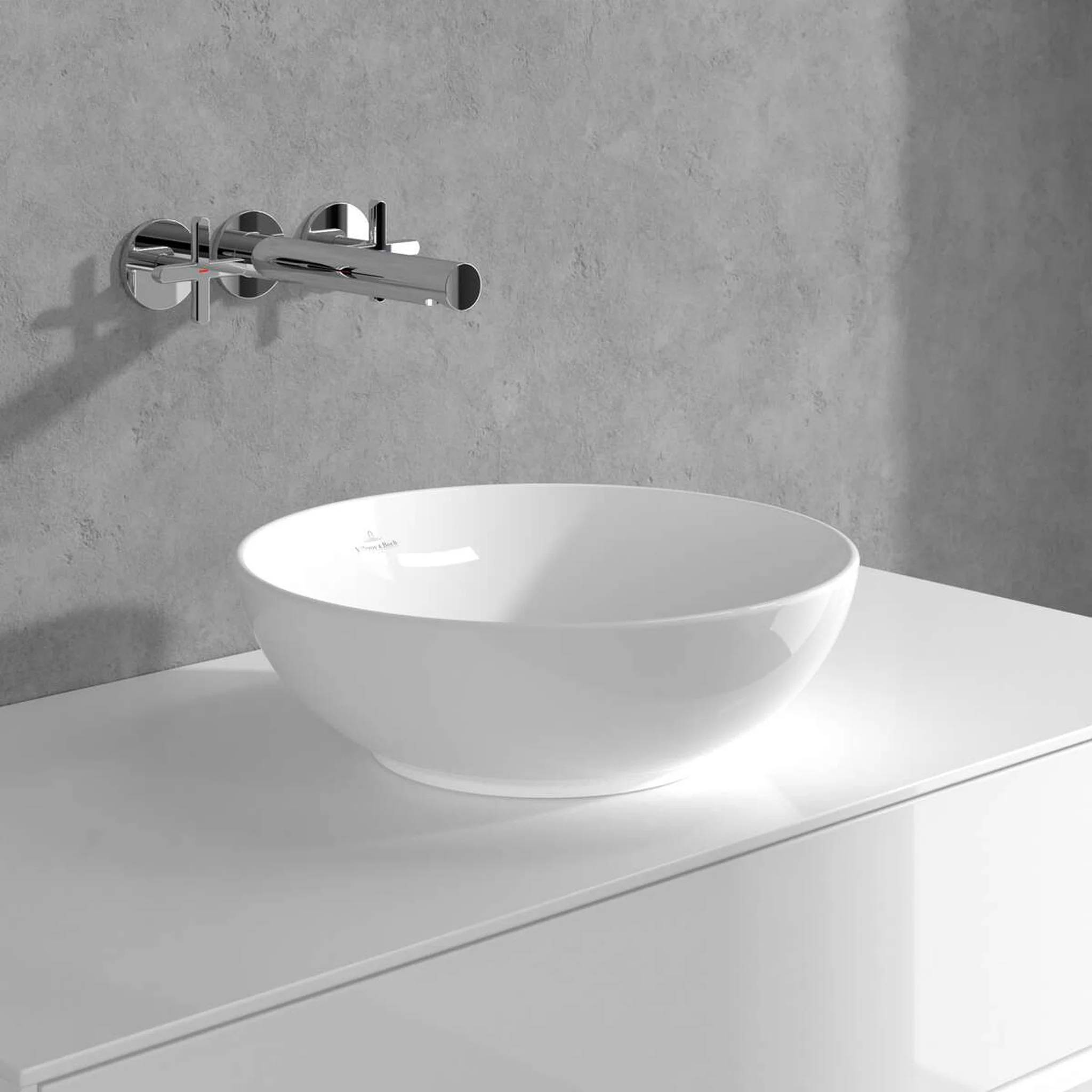 Minimalistisches Badezimmerbecken mit einem weißen Aufsatzwaschbecken auf einer Arbeitsplatte und einem an der Wand montierten Chromwasserhahn vor einer grauen Wand.
