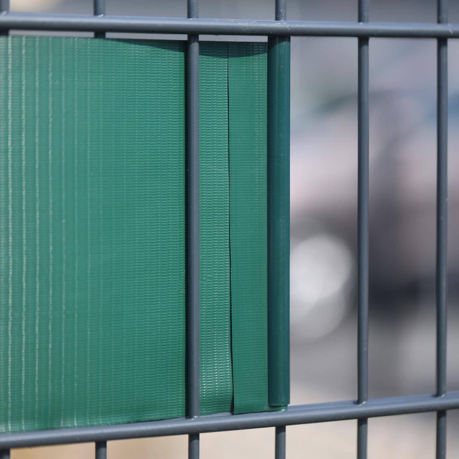 Grüner Sichtschutz, der an einem grauen Metallzaun befestigt ist und die Sicht dahinter teilweise verdeckt.