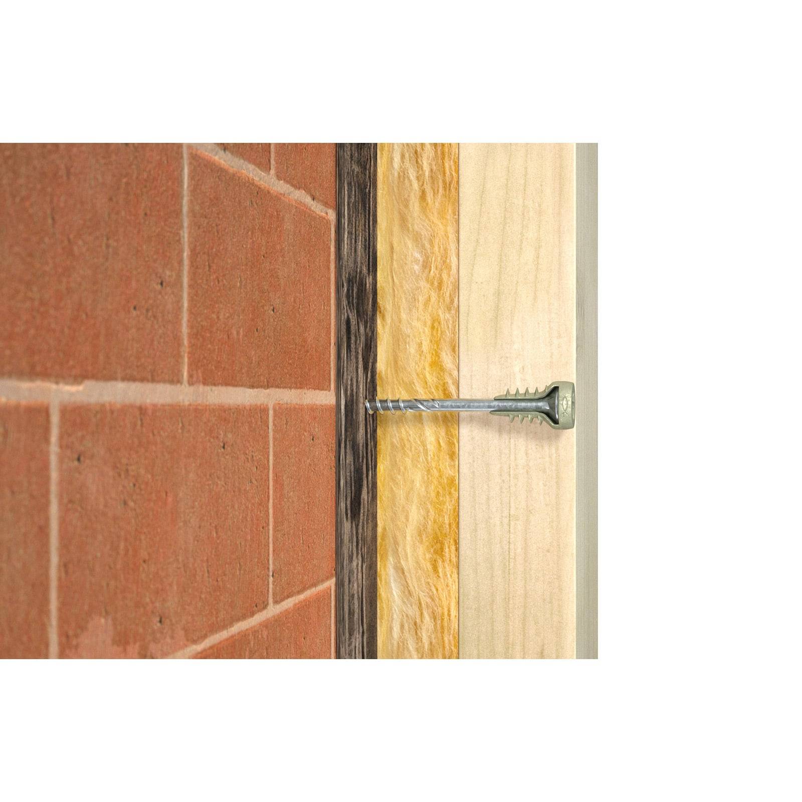 Querschnittsdarstellung einer Wand mit einer Schraube, die durch Ziegel, Dämmung und Holzpaneele hindurchdringt.