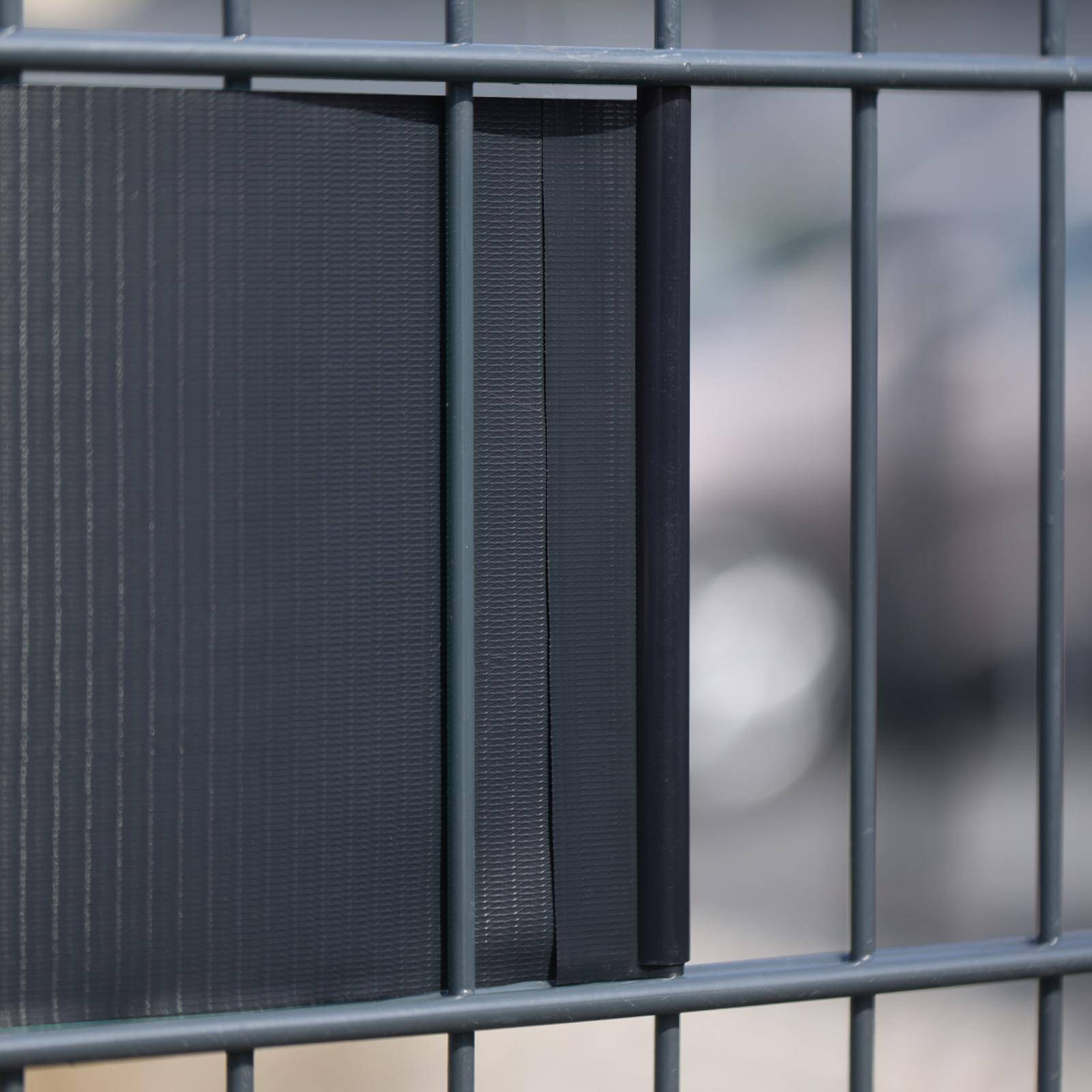 Nahaufnahme eines dunklen Metallzauns mit vertikalen Stäben und Maschenpaneel, mit unscharfem Hintergrund dahinter.