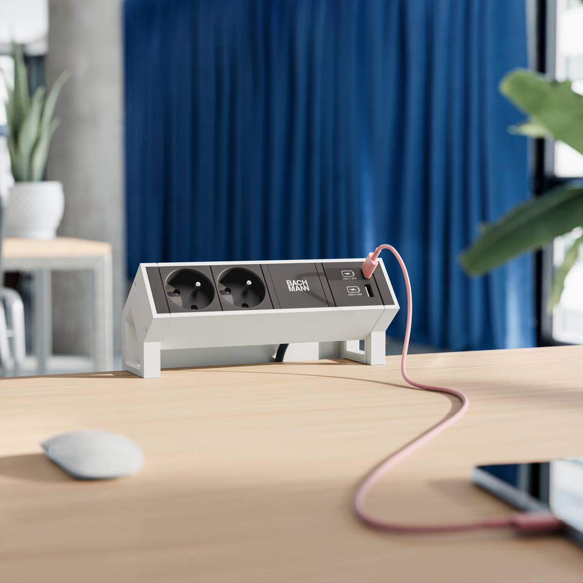Mehrfachsteckdose auf dem Schreibtisch mit zwei Steckdosen und USB-Anschlüssen auf einem Holztisch, ein Anschluss mit einem rosa Ladekabel verbunden.