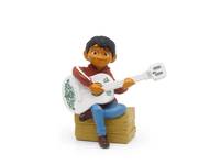 Kleine Figur eines lächelnden Kindes, das eine weiße Gitarre spielt, während es auf einer Holzkiste gegen einen einfachen Hintergrund sitzt.