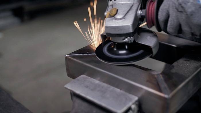 Ein Arbeiter verwendet eine Winkelschleifmaschine an Metall und erzeugt helle Funken. Das Bild konzentriert sich auf die kreisförmige Klinge des Werkzeugs und die nach außen fliegenden Funken.