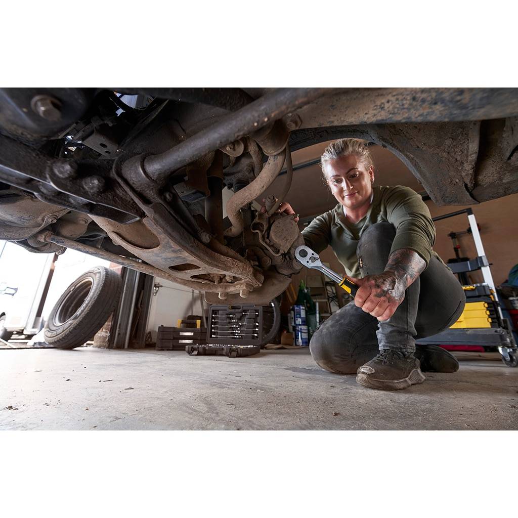 Mechaniker kniet unter einem Fahrzeug in einer Werkstatt und repariert mit einem Schraubenschlüssel die Aufhängung oder das Fahrwerk.