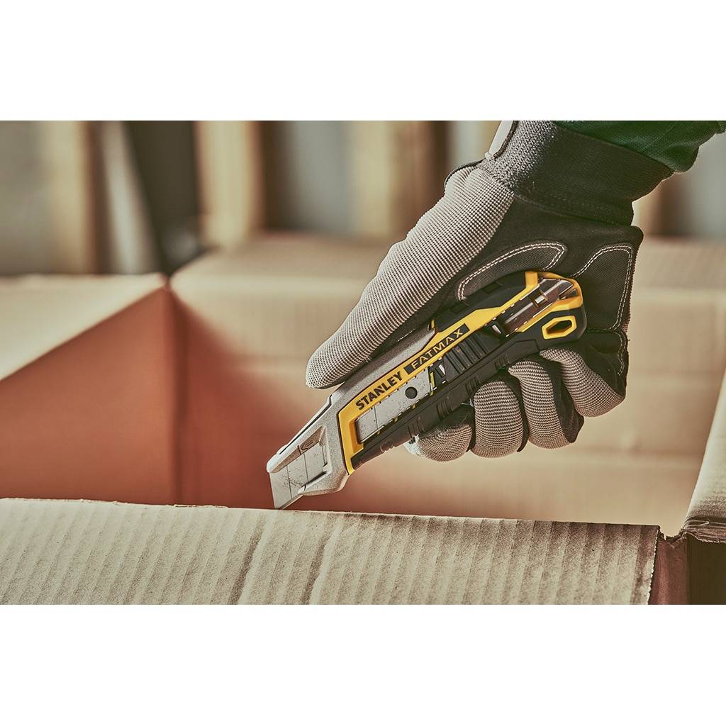 Behandschuhte Hand hält ein Stanley-Universalmesser über gewellter Pappe, bereit, eine Schachtel zu öffnen.